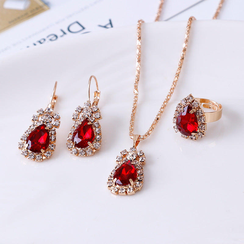 Rhinestone jewelry set featuring red teardrop earrings, necklace, and ring in gold finish